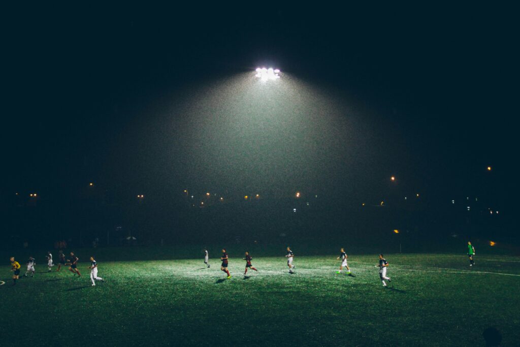 Soccer field at night with two teams having courage playing soccer